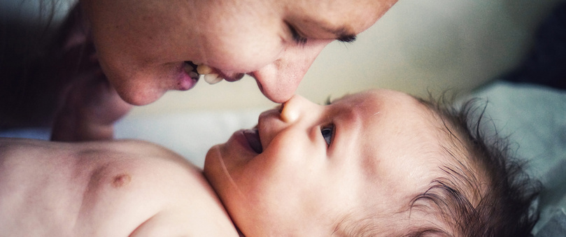 Humana Baby lächelt Mama an